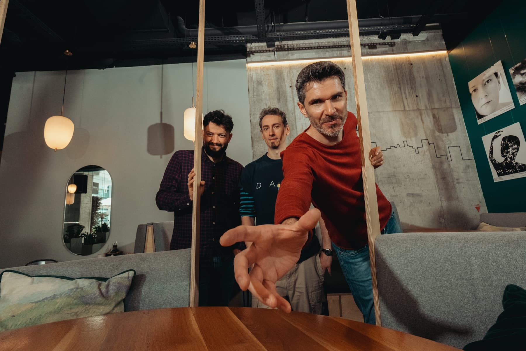 Membrii trupei într-o cafenea, unul întinzând mâna spre cameră